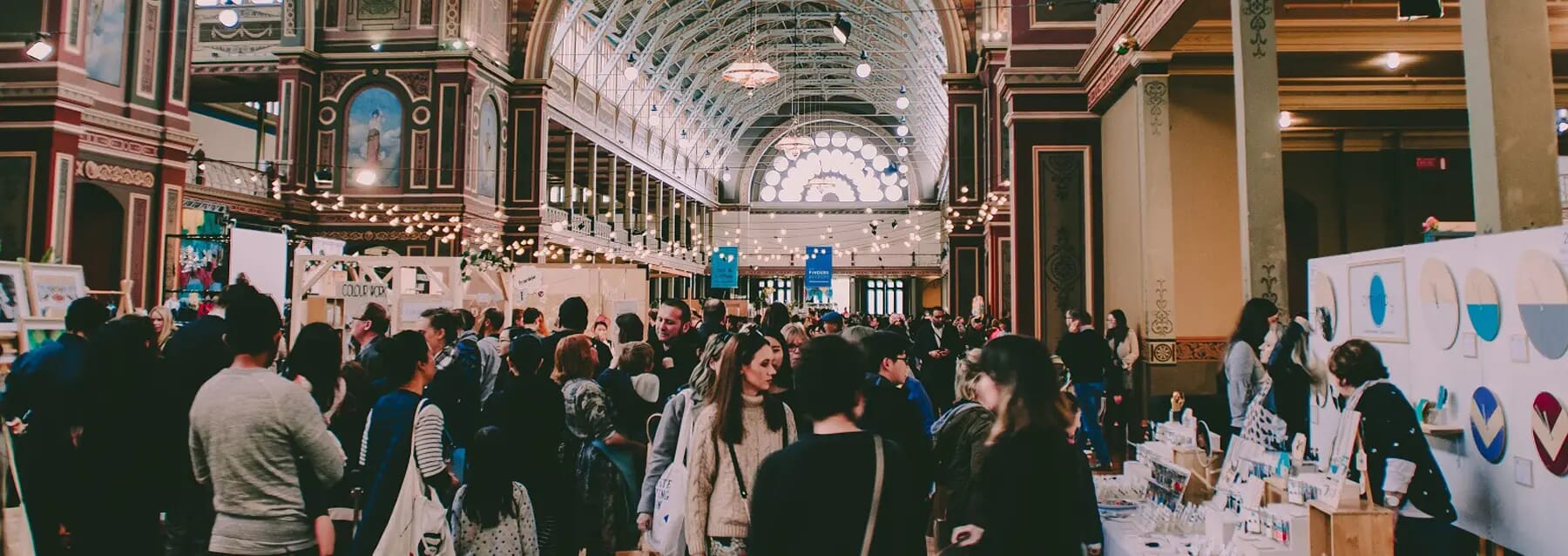 Crowd of people looking at booths in a large and ornate trade show hall