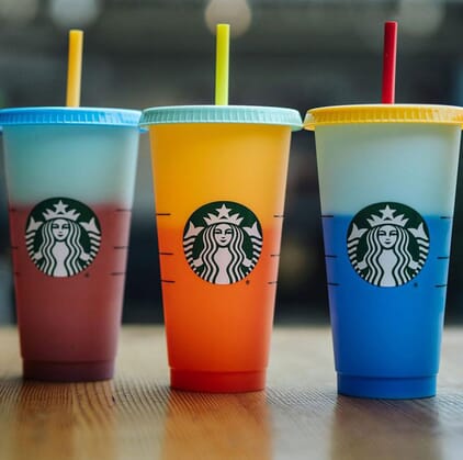 Five Starbucks color-changing cups in various colors on a wooden tabletop