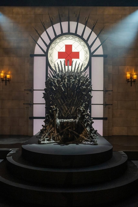 Iron Throne made from a multitude of swords, with a stained glass image of the American Red Cross logo above its back