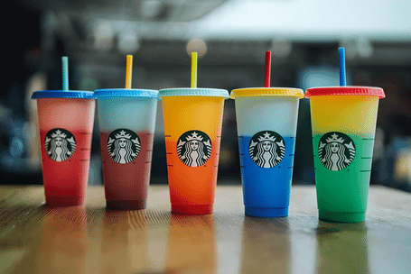 Five Starbucks color-changing cups in various colors on a wooden tabletop
