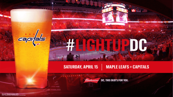Beer glass with red light-up base in front of a crowded hockey stadium, with the hashtag 'light up DC'