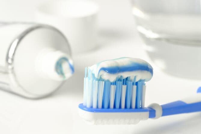 Blue and white toothbrush with blue and white toothpaste on white countertop next to tube of toothpaste.