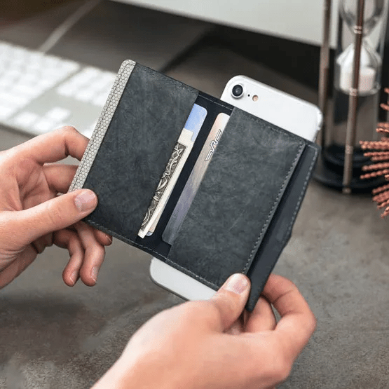 Person's hands holding a black folding phone wallet attached to the back of a white iPhone