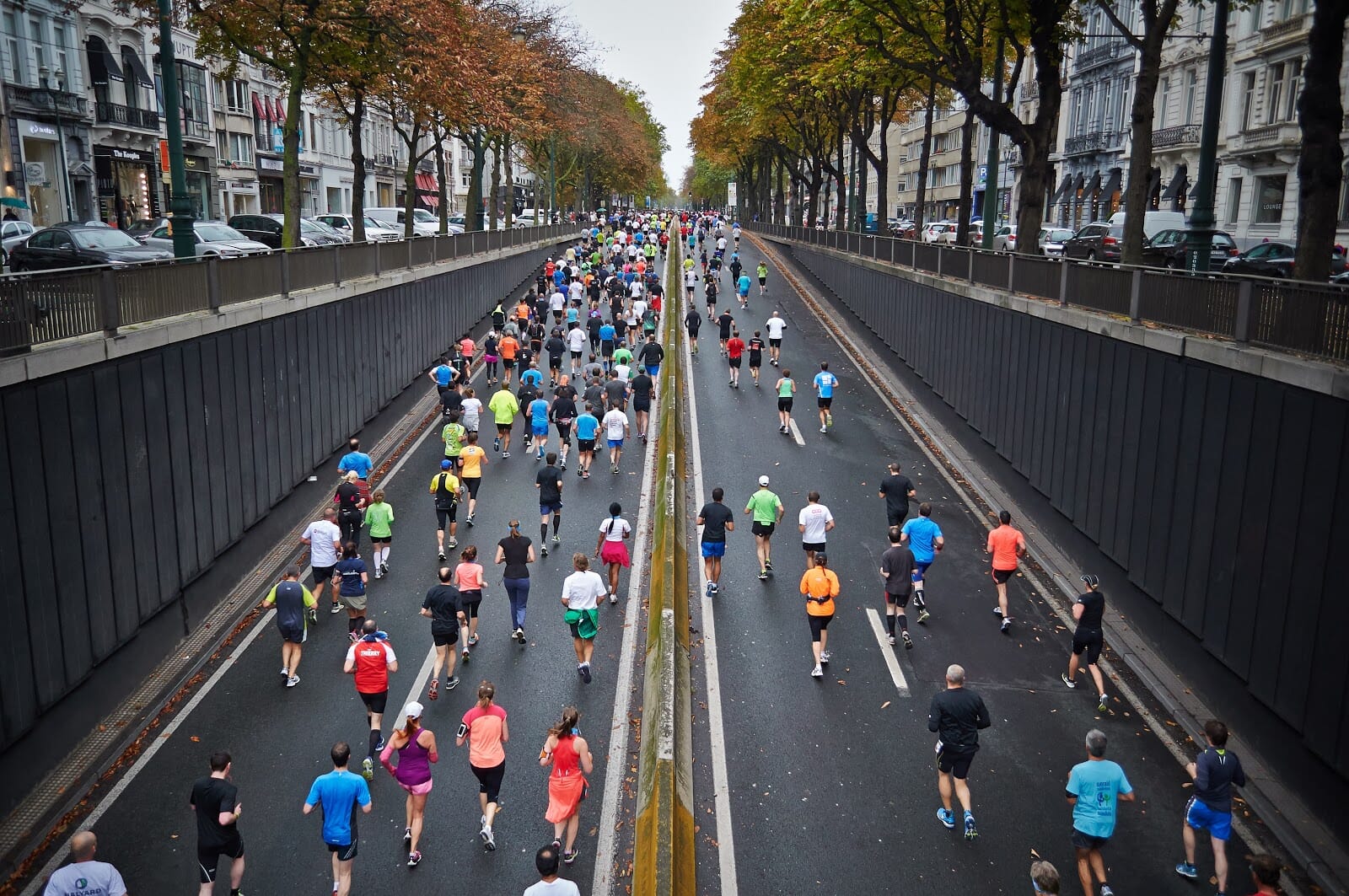 Crowd of people in brightly colored shirts running up a road during a marathon