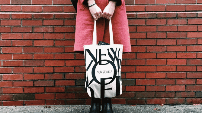 Woman walking across red, black and white stone plaza carrying two branded canvas tote bags