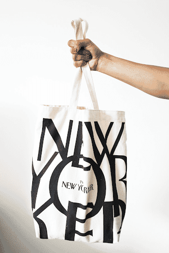 Woman's hand holding a New Yorker tote bag in front of a white wall