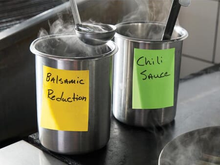 Two steaming stainless steel pots in an industrial kitchen, each labeled with a Post-it Extreme Sticky Note