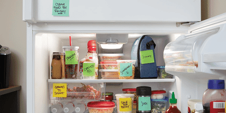 Various food containers in an office fridge, each labeled with a Post-it Extreme Sticky Note
