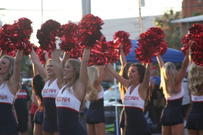 Group of cheerleaders wearing red, white and black uniforms while shaking red pom poms