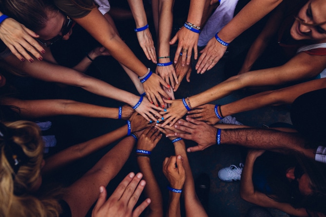 Aerial view of group of people standing in a circle wearing blue silicone bracelets putting their hands together
