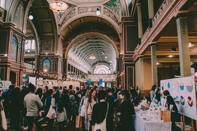 Crowd of people looking at booths in a large and ornate trade show hall.