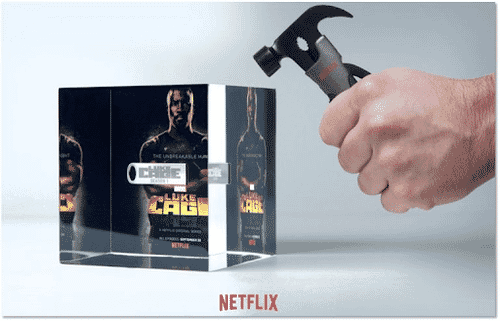 Man's hand holding hammer above clear Luke Cage-branded cube containing a USB drive
