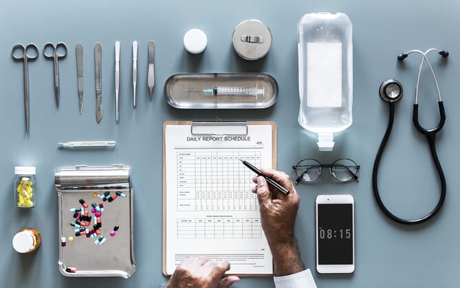 A table with medical tools and supplies, some medicine, a cellphone, and a clipboard with a report schedule on it